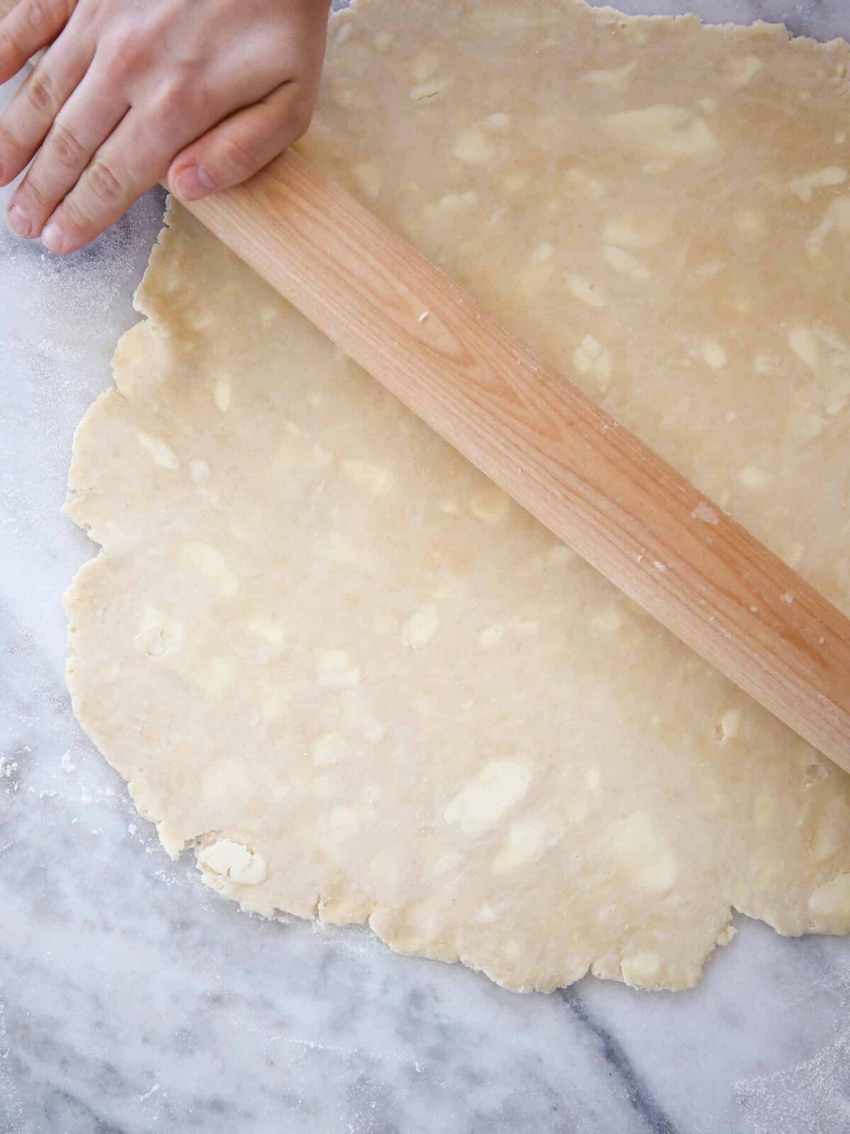 vodka pie dough rolled on marble with rolling pin and hands. 