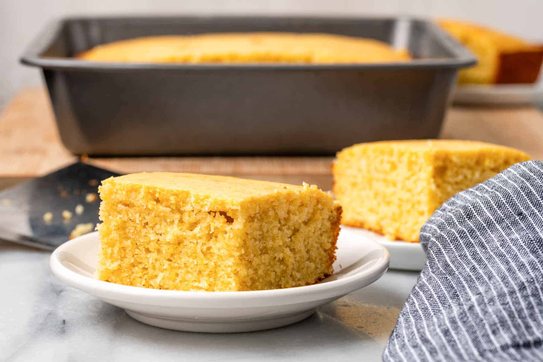 sweet cornbread slices on white plates with baking dish in background.