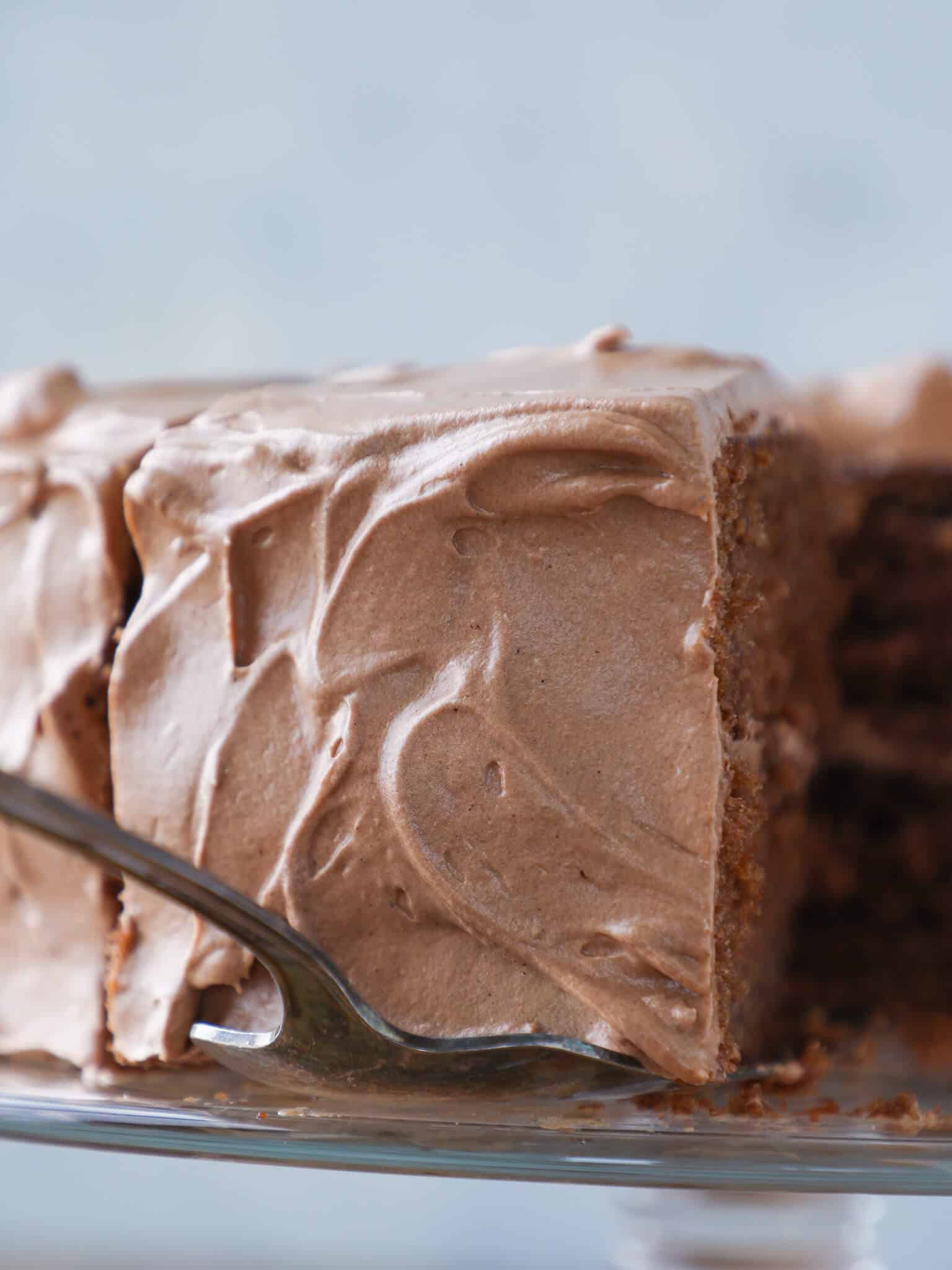 Old Fashioned Chocolate Fudge Cake slice being served with icing swirls.