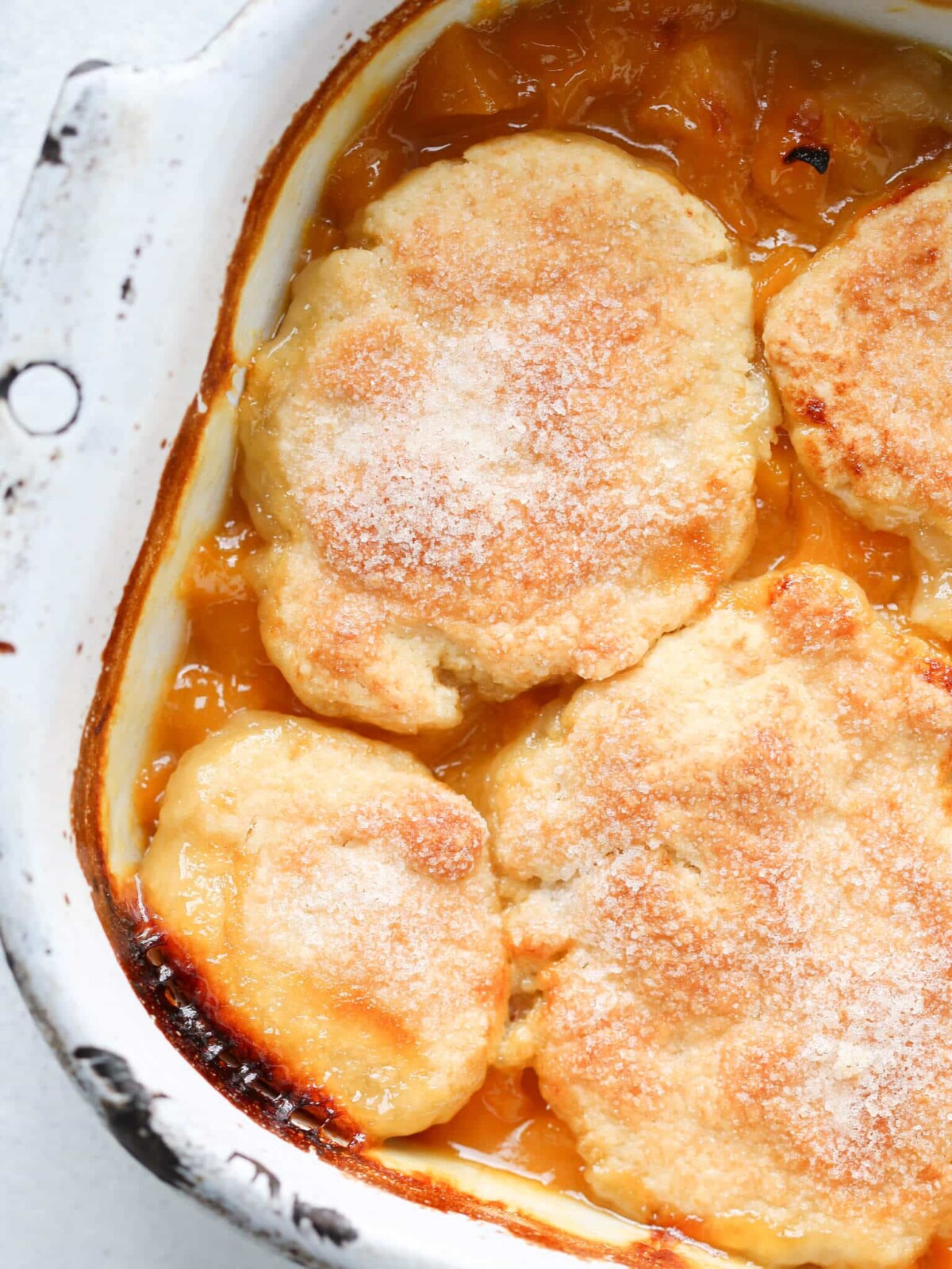 Old Fashioned Peach Cobbler sugared biscuit topping in white vintage dish.