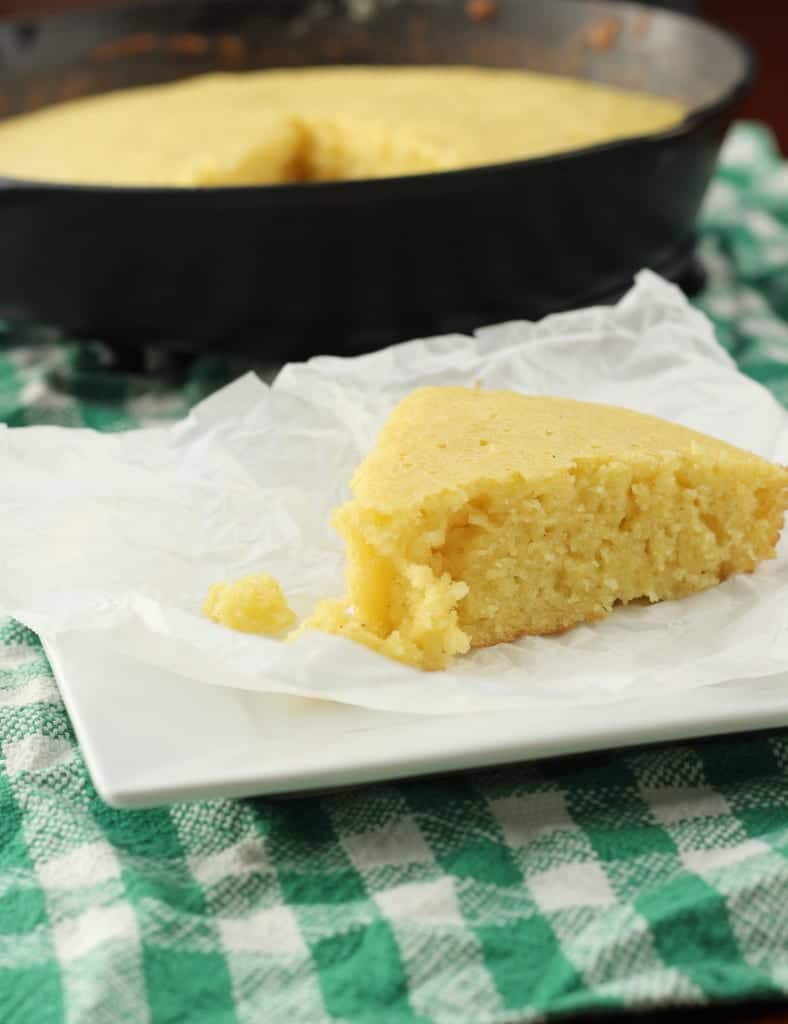 slice of cornbread baked in cast iron skillet on green towel.