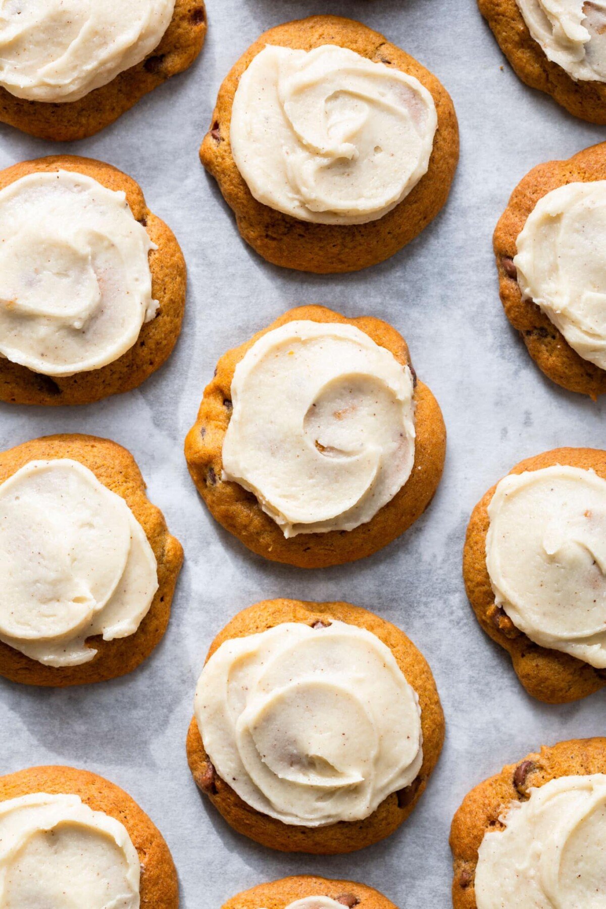 iced pumpkin cookies baked on parchment.