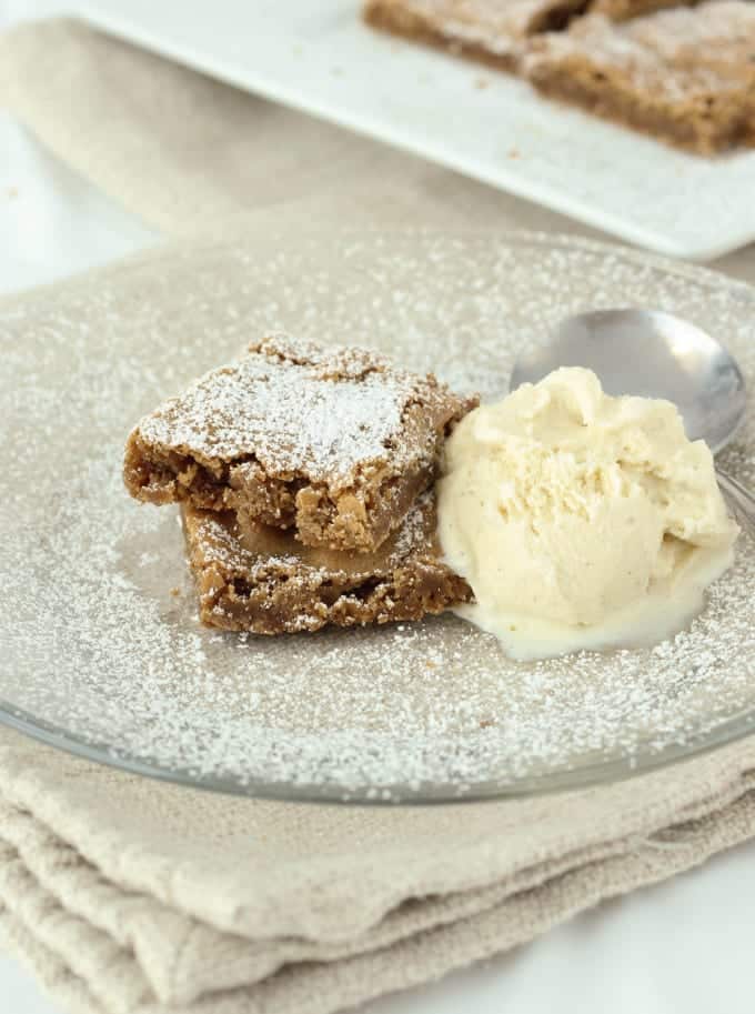 Two butterscotch brownies served on a clear plate with a scoop of vanilla ice cream.