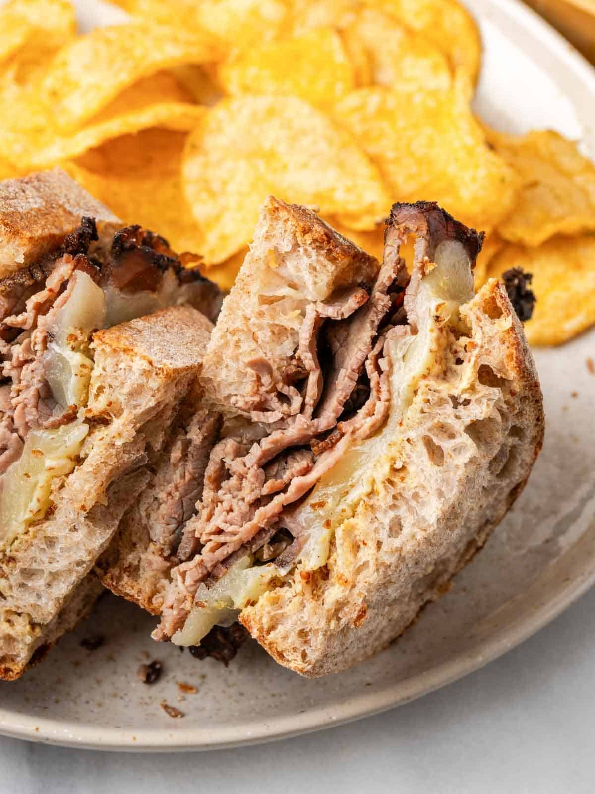 roast beef sandwich halves on plate with chips.