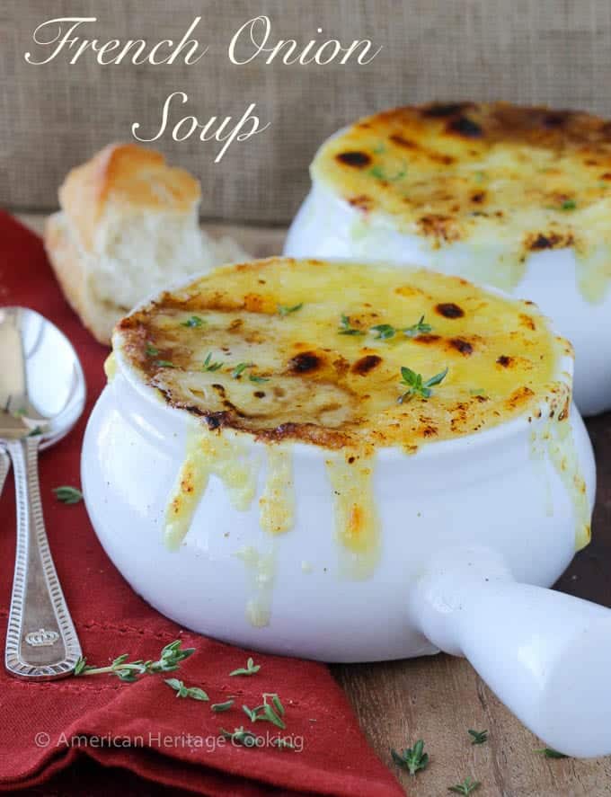 French onion soup in a white bowl with little fresh thyme leaves on top.