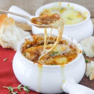 French onion soup in a white bowl with silver spoon pulling cheese.