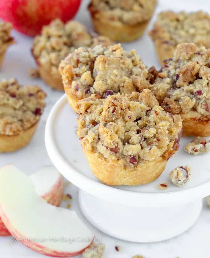 mini apple pies with pecan crumble on top on small white cake stand. 