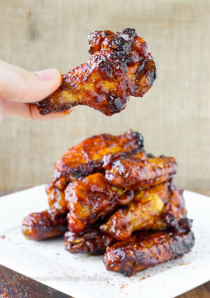 A stack of baked chicken wings with one wing being held up.