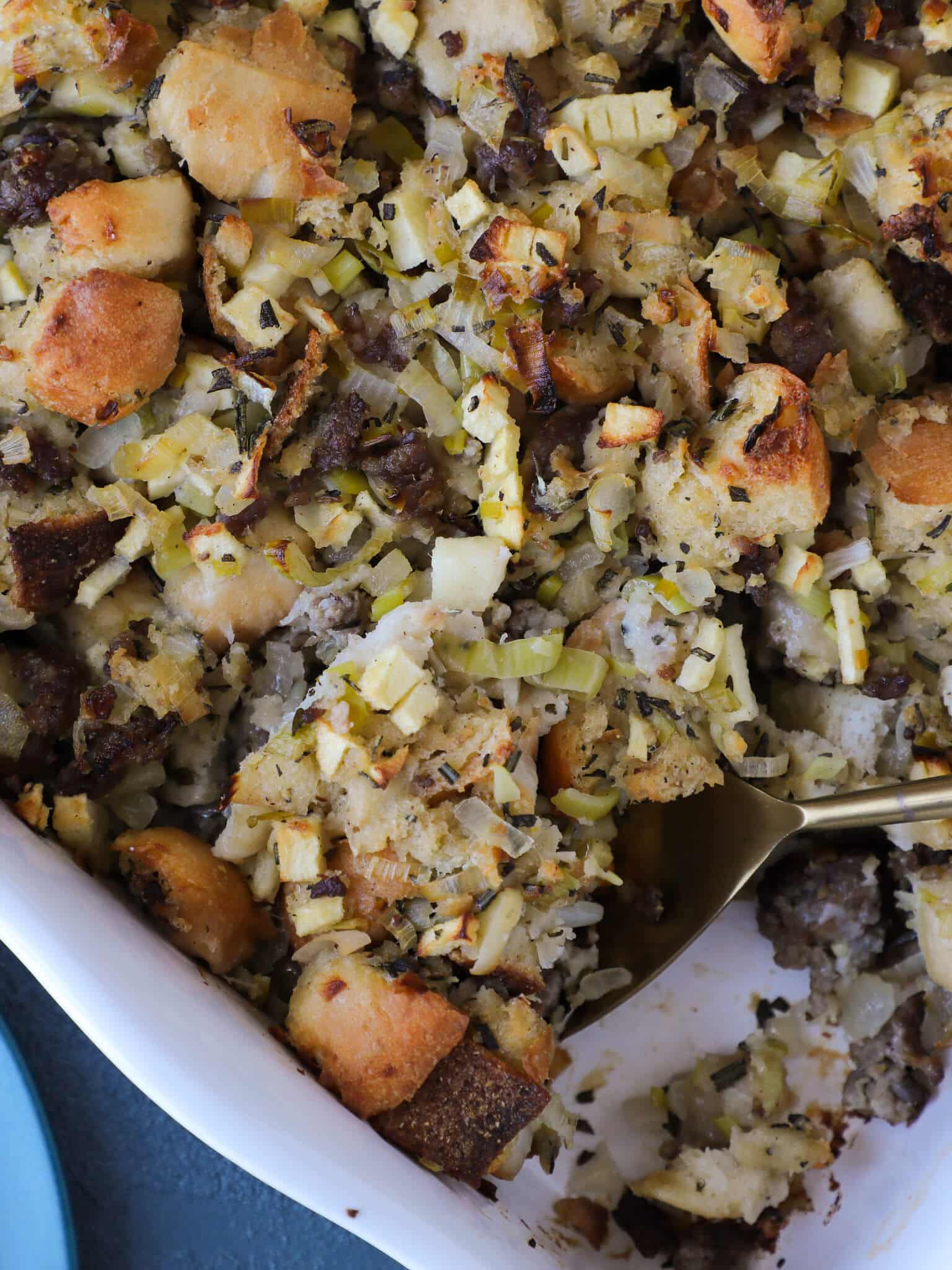 Apple Sage Sausage Stuffing in a white baking dish with a spoon.