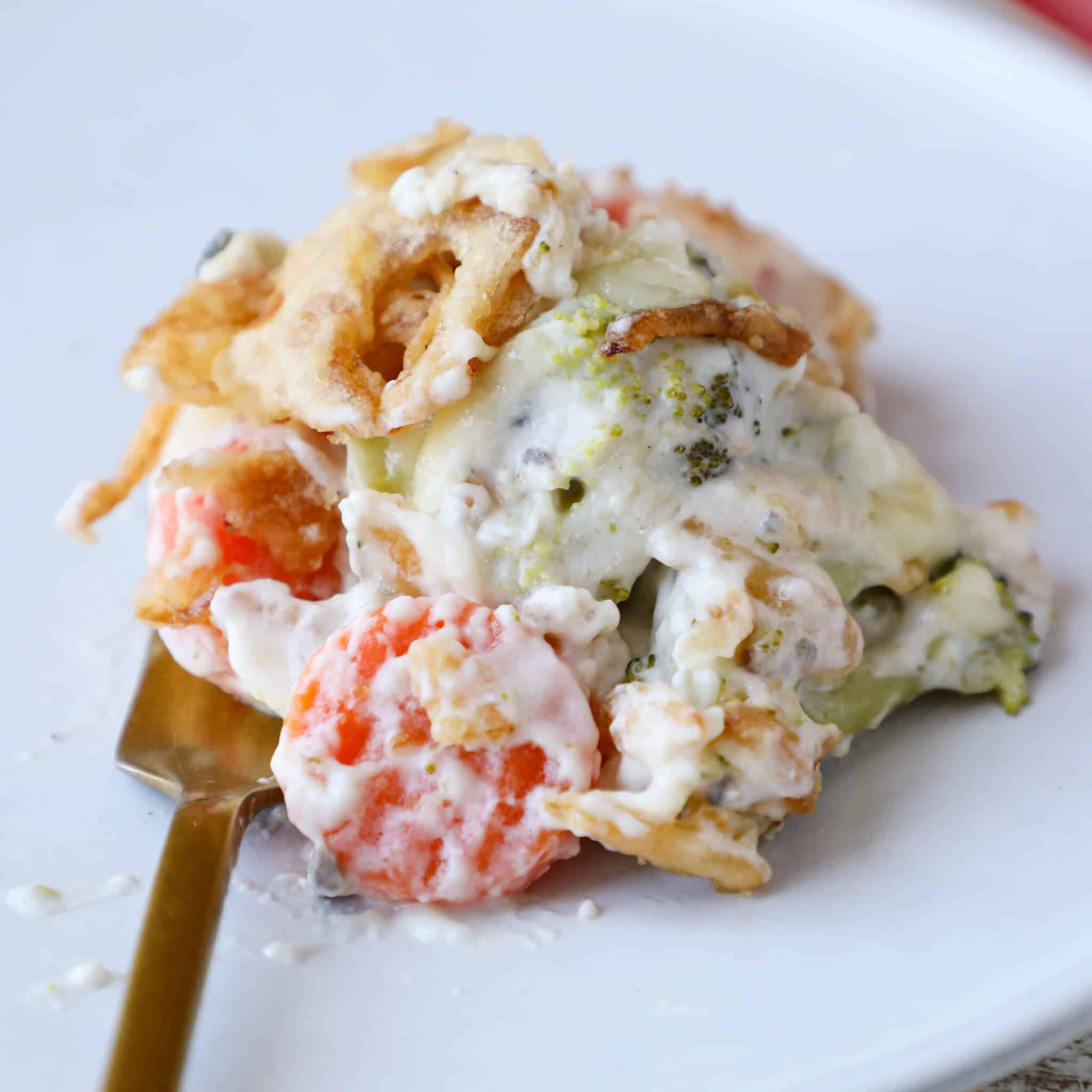 A serving of vegetable casserole on a white plate with a gold fork.