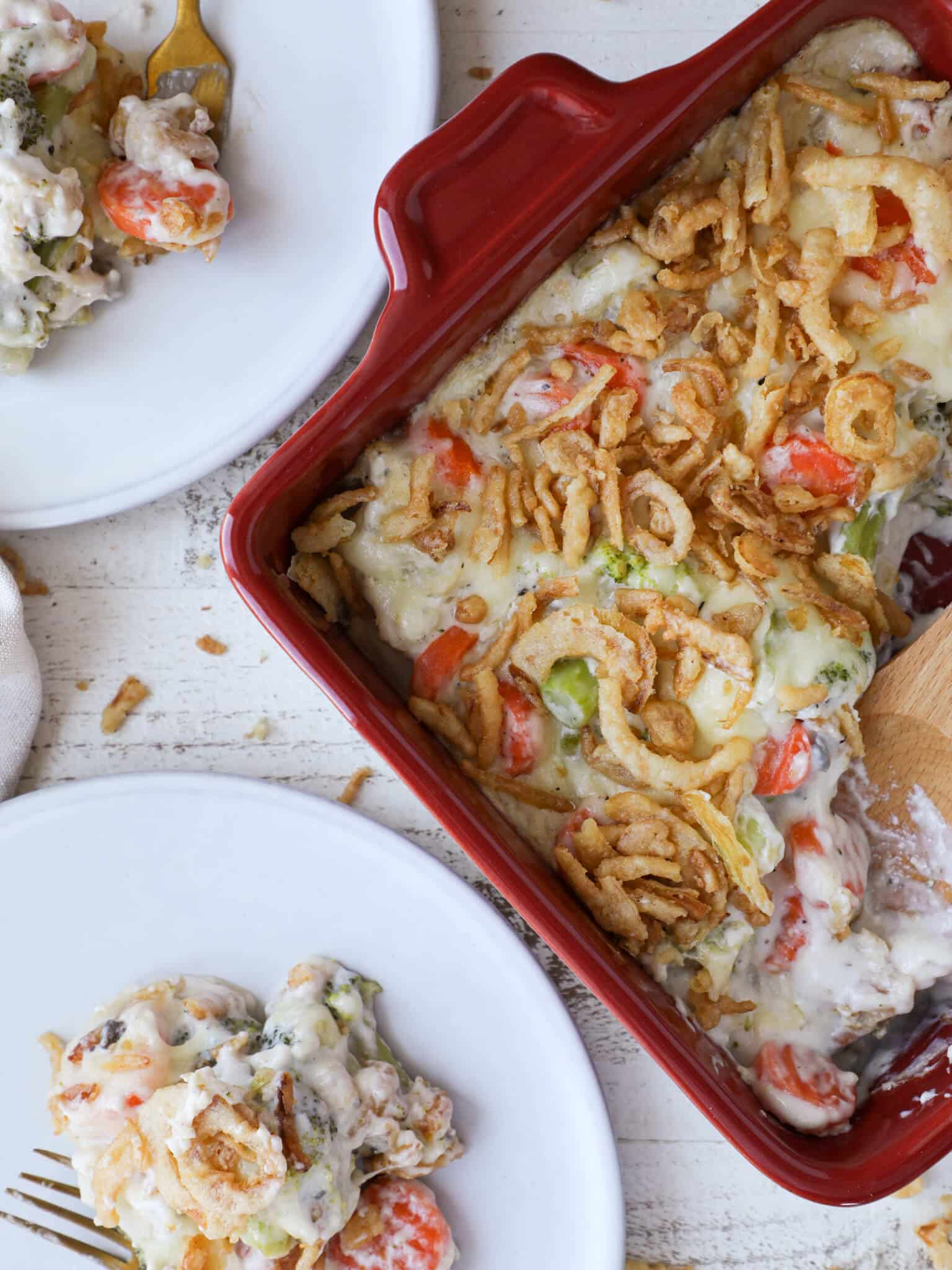 Vegetable casserole served in a red baking dish with two white plates.