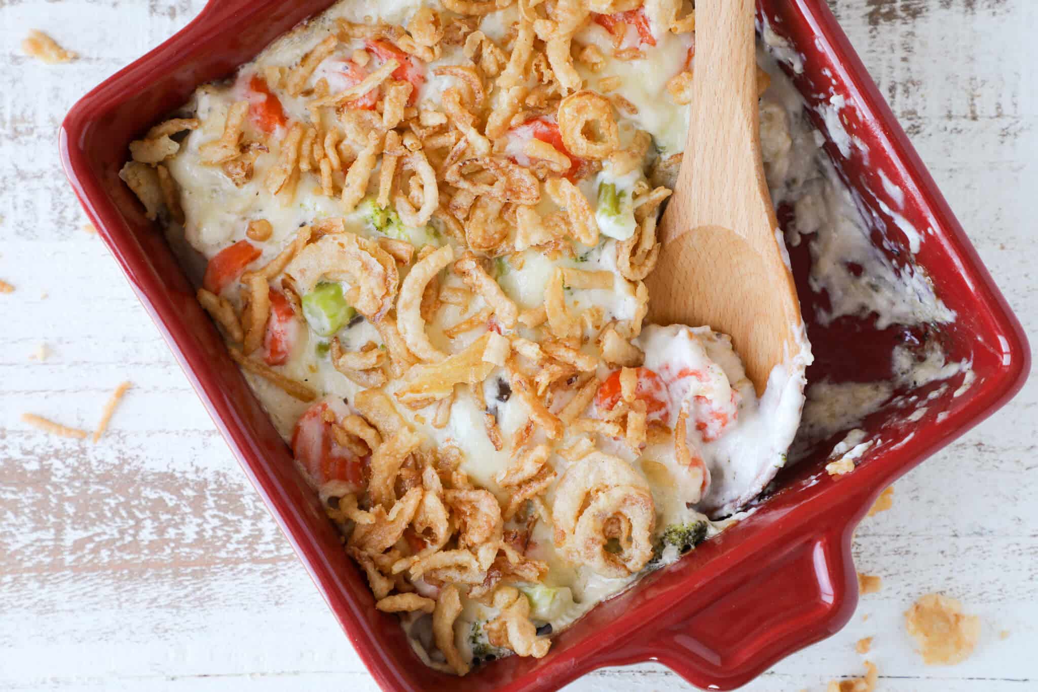 Baked vegetable casserole in a red dish with crunchy onions on top.