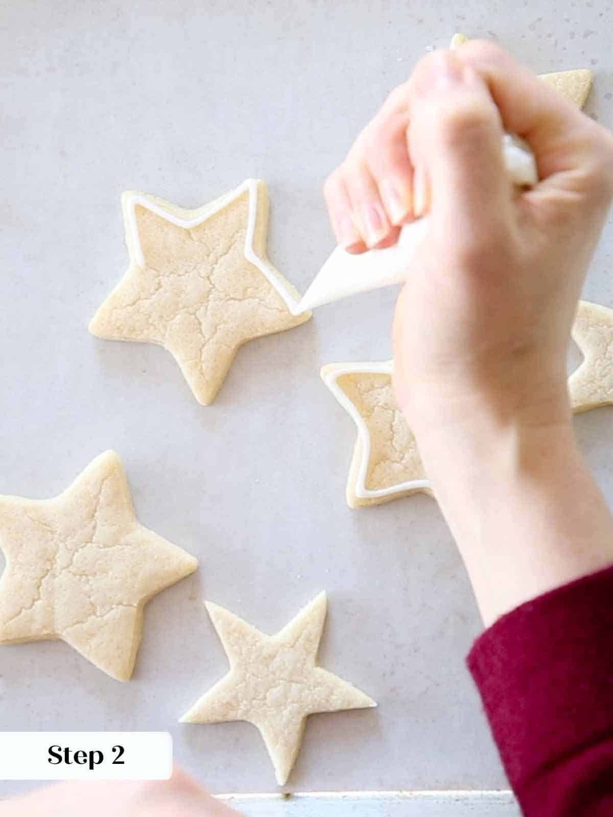 outlining white royal icing on sugar cookie stars.