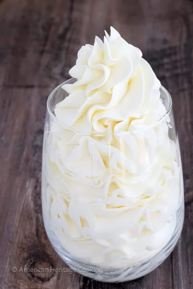Italian meringue buttercream in a clear glass against a wooden backdrop.