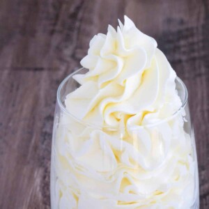 Italian meringue buttercream cleanly piped into a clear glass with a little sticking out of the top.