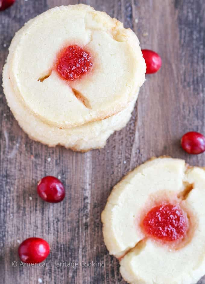 two cranberry thumbprint cookies on wooden board.