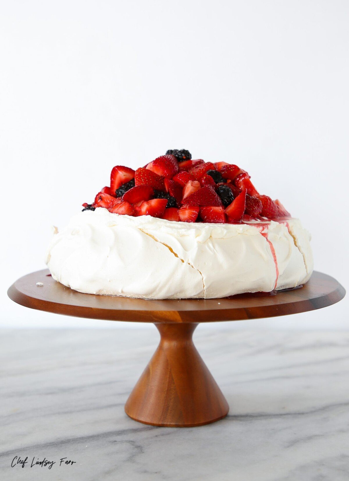 pavlova with fruit on a wooden cake stand. 