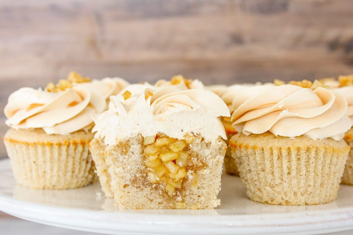 Cake stand full of caramel apple cupcakes one sliced in half to show apple filling.