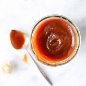 apple butter in clear jar with spoon on marble.