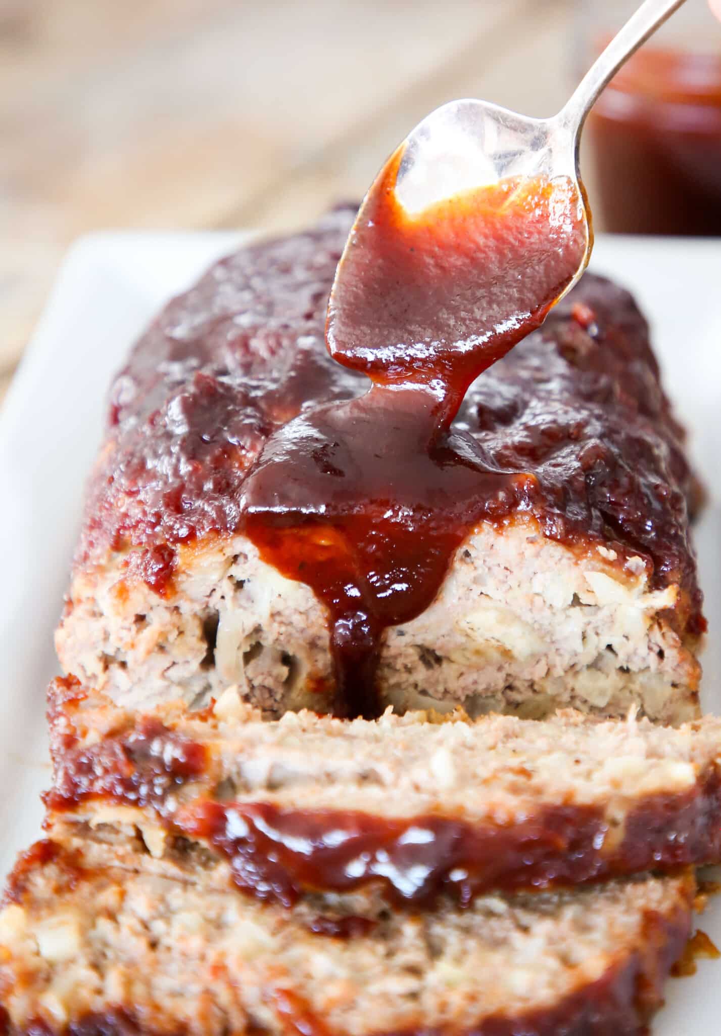 Sliced meatloaf with brown sugar sauce pouring over the top.