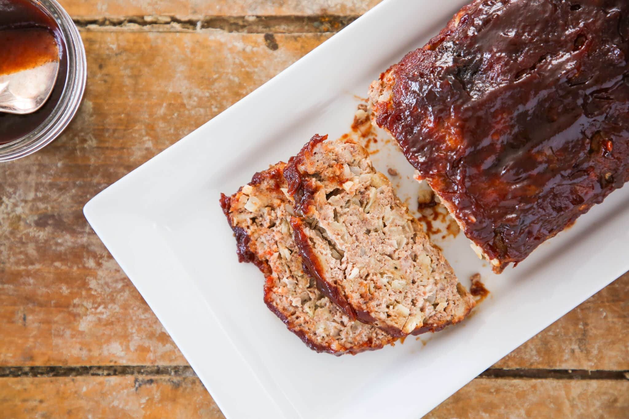 Meatloaf with two slices sliced off over a white plate on a wood slate background.
