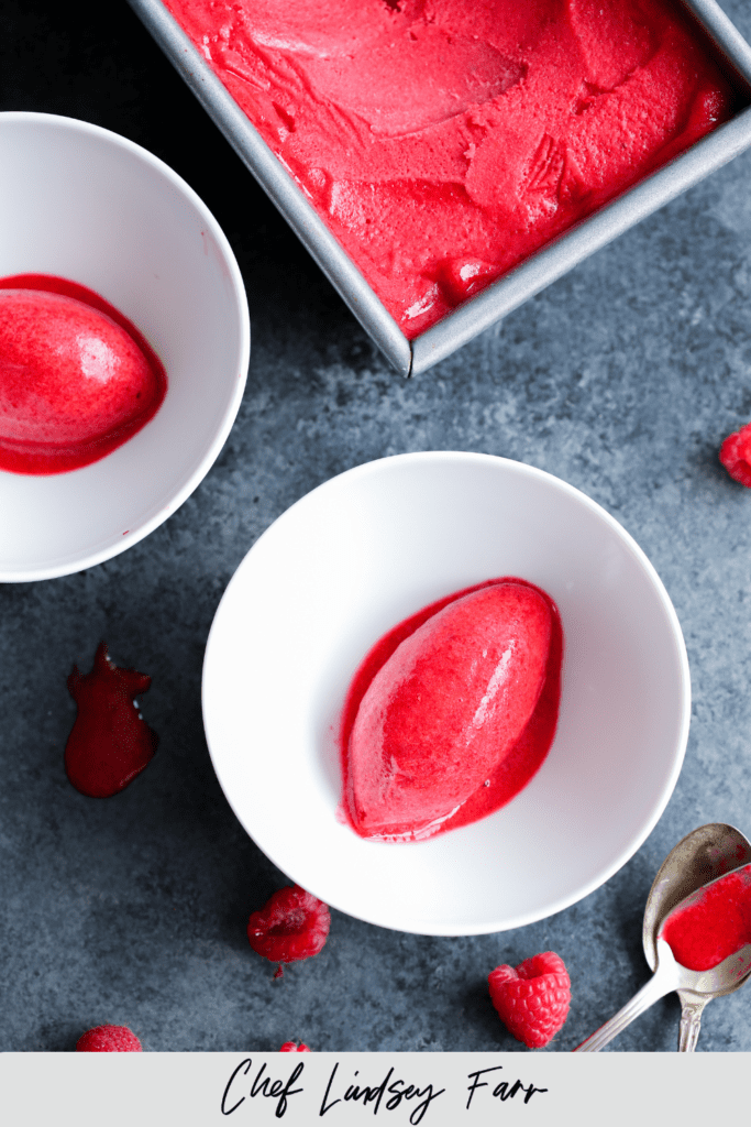 Raspberry Sorbet in two white bowls with silver spoons on the table.