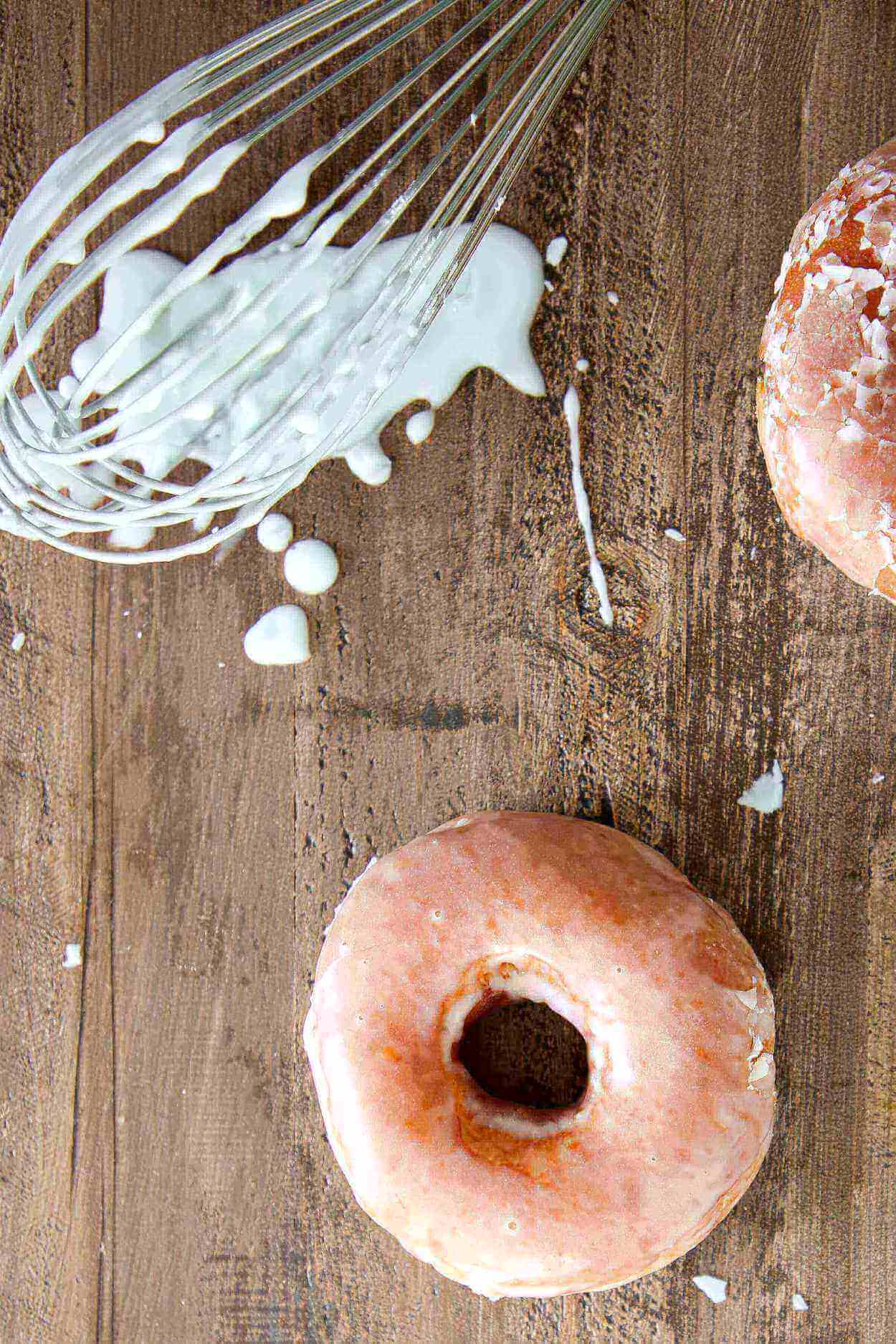 Doughnut glaze dripping off of a whisk onto a wood slate background.