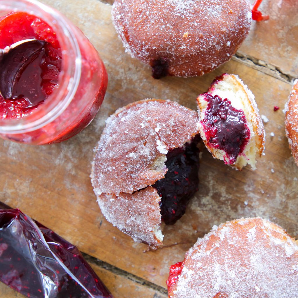 yeasted donut with berry jam broken open on a wooden surface. 