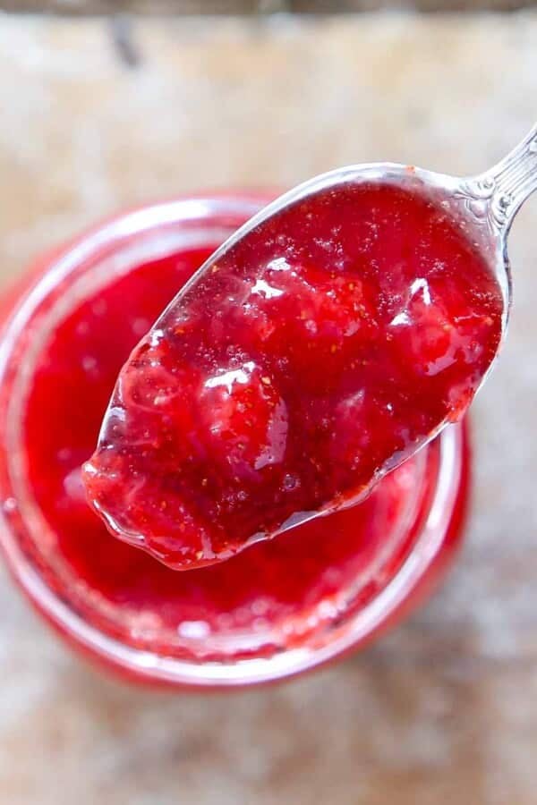 strawberry jam on large spoon held over jar.