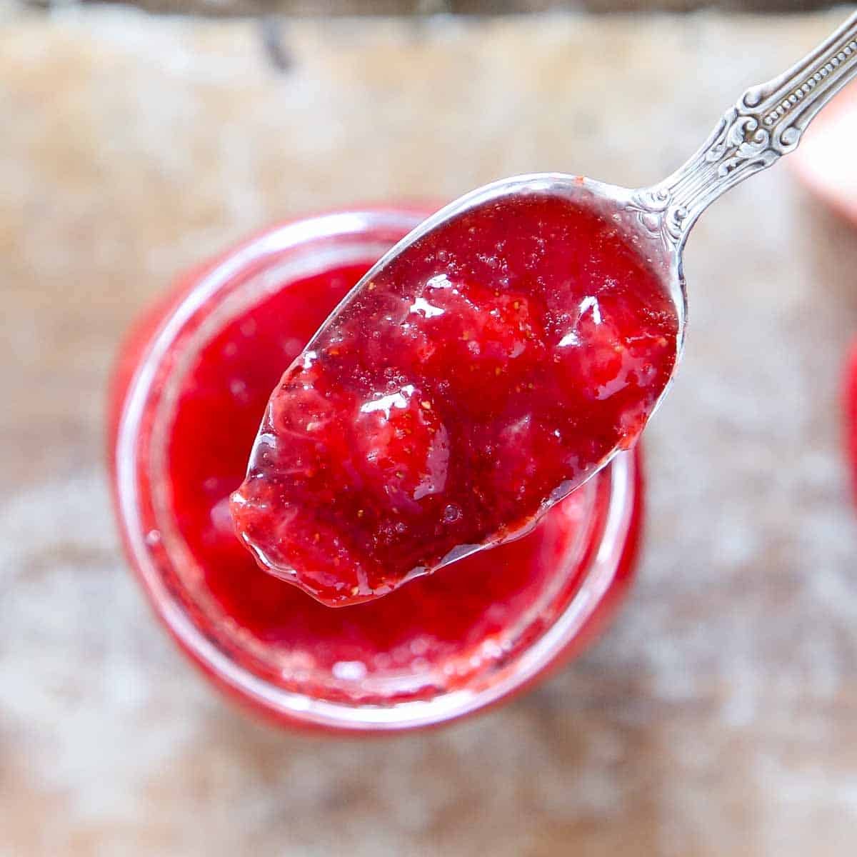strawberry jam on large spoon held over jar.