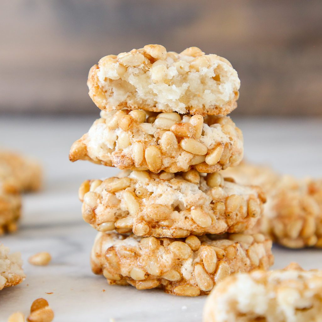 A stack of 4 pignoli cookies studded with pine nuts.