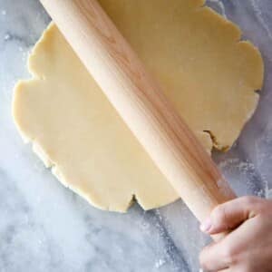 pate sucree dough disk being rolled by wooden pin on marble.