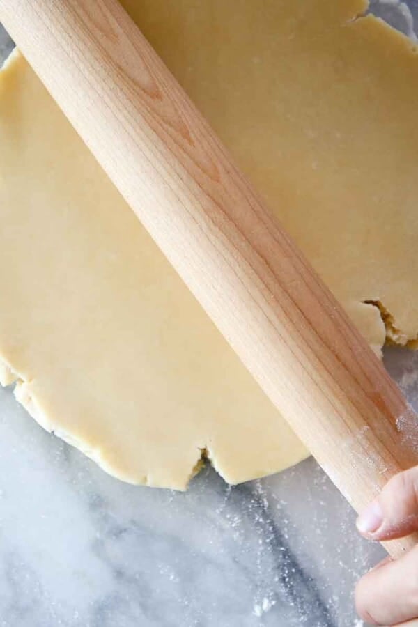 pate sucree dough disk being rolled by wooden pin on marble.