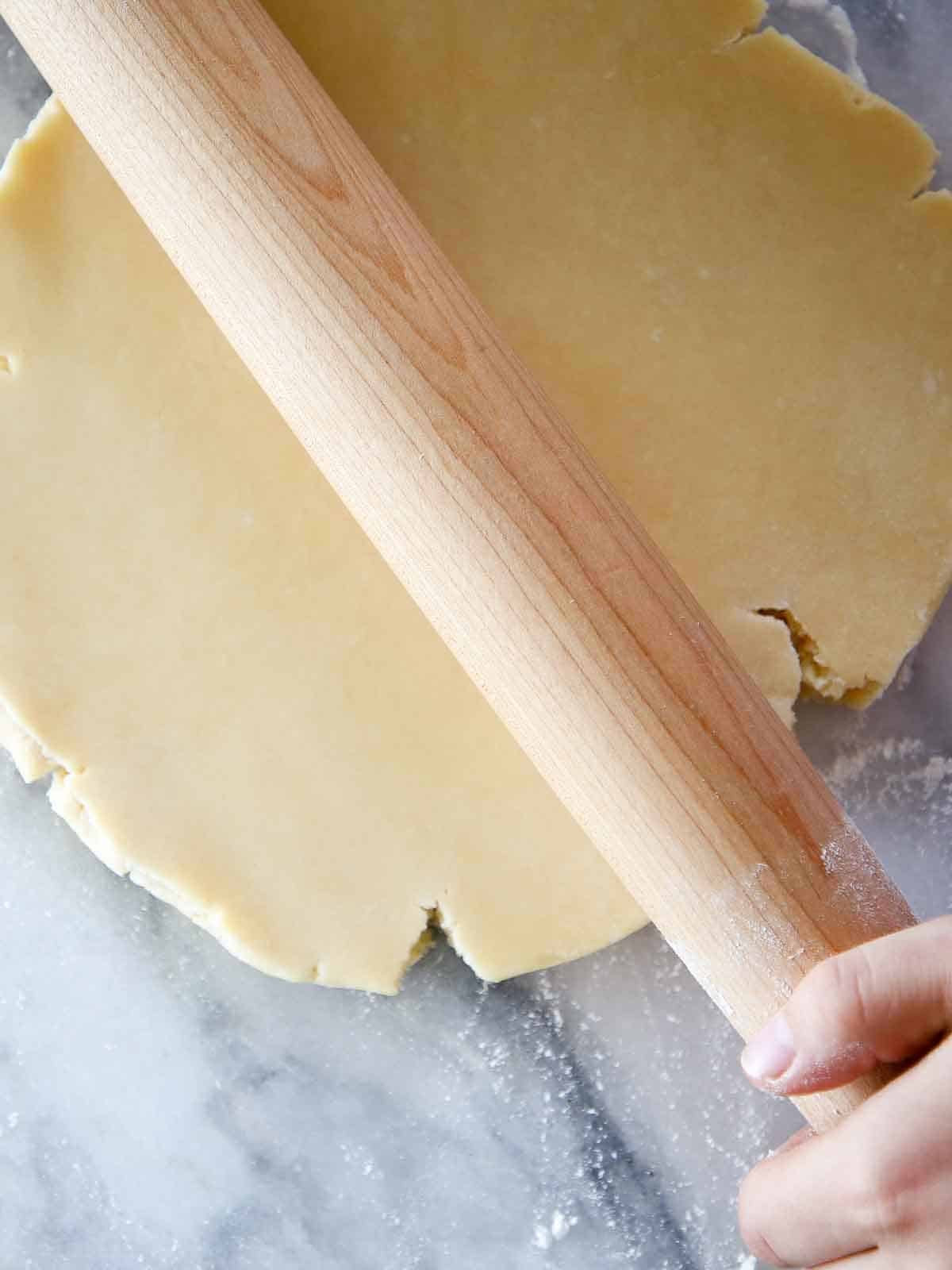 pate sucree dough disk being rolled by wooden pin on marble. 