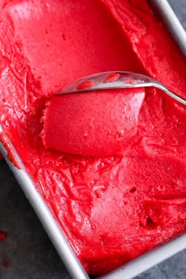 Raspberry Sorbet being scooped with a silver spoon.