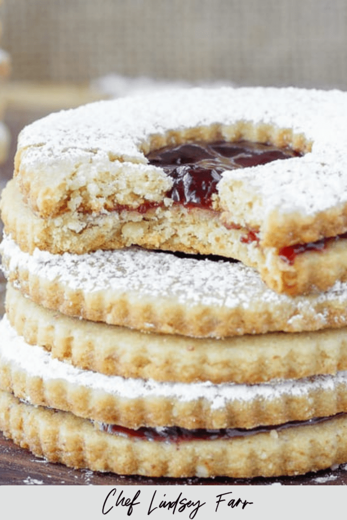 A stack of raspberry linzer cookies with the top one bitten.