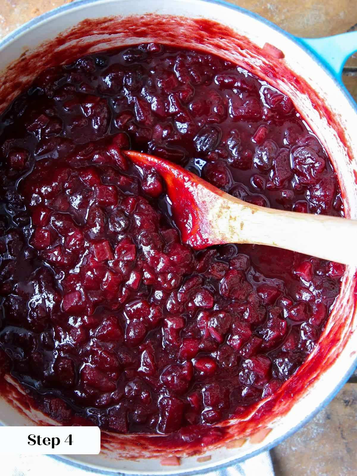 cooked cranberry chutney in pot with wooden spoon.