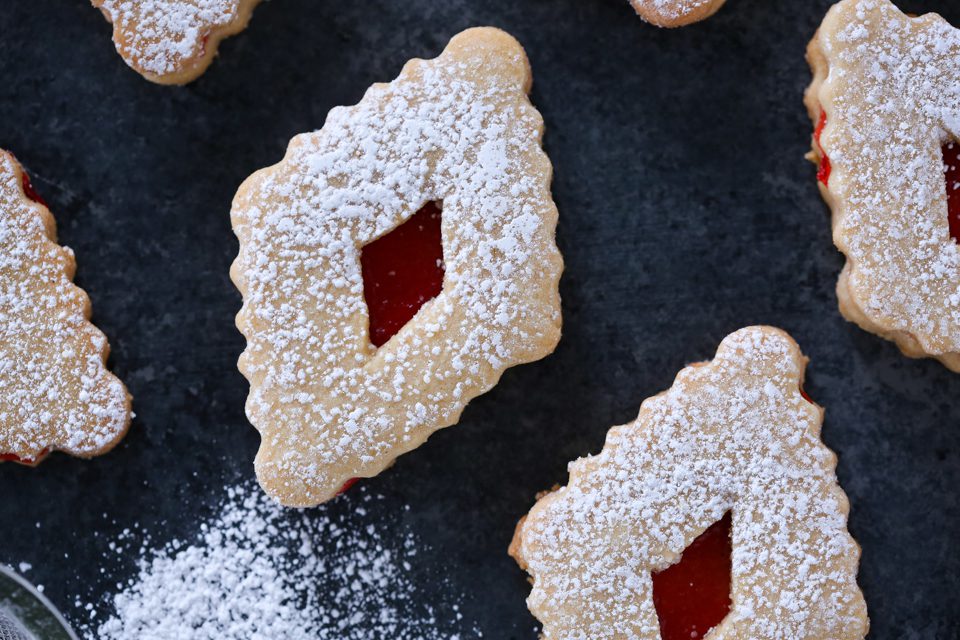A group of linzer cookies on a dark background with their edges perfectly wavy.