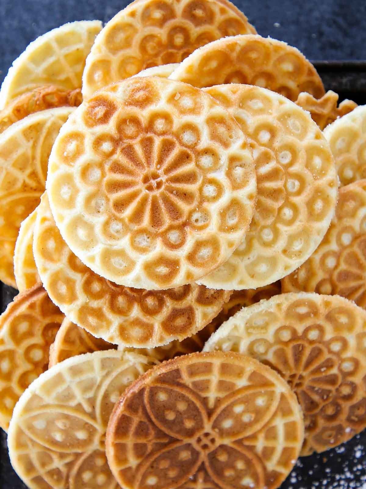 pizzelle cookies piled on a black tray.