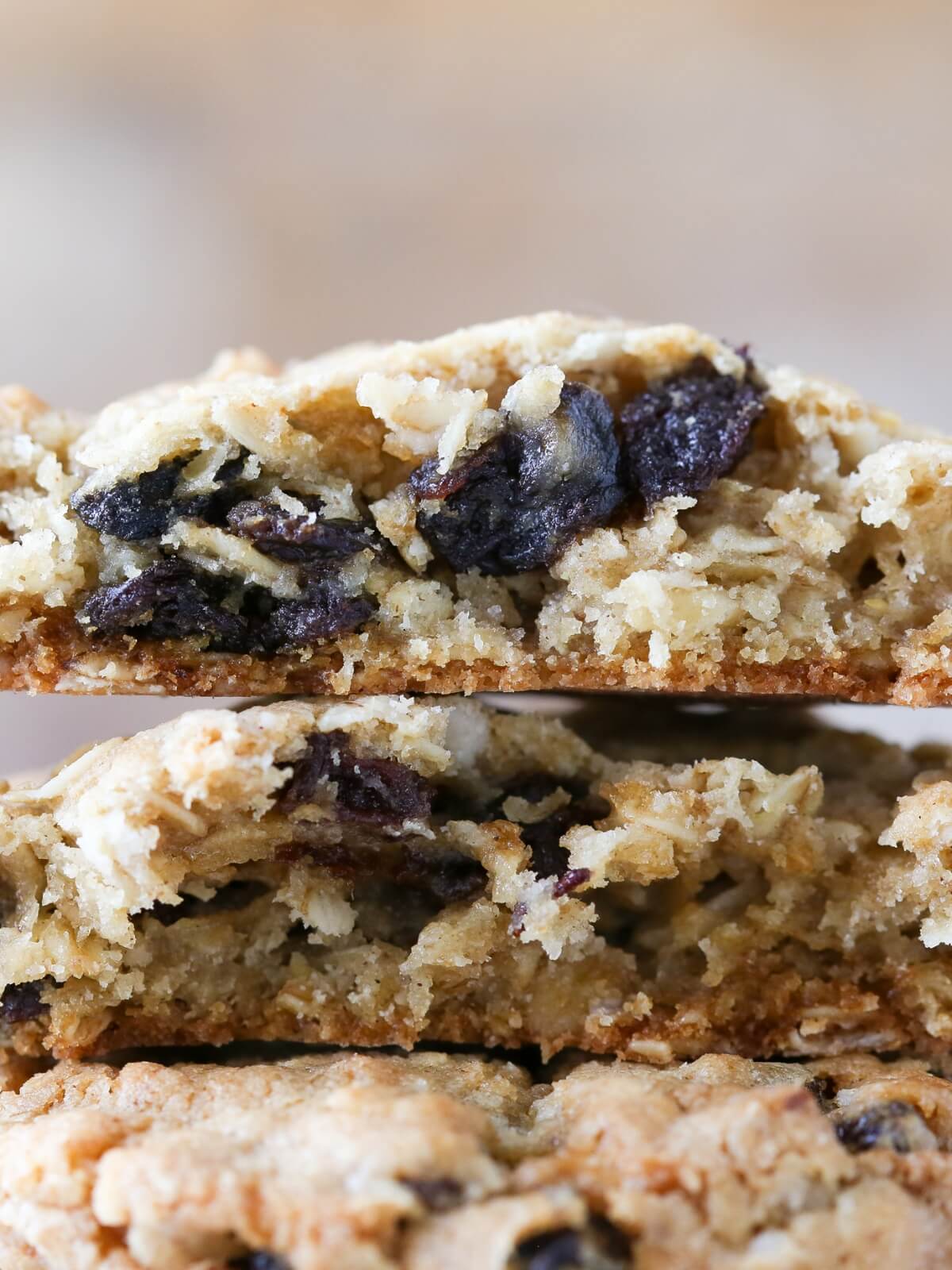 A stack of three oatmeal raisin cookies with the top ones cut in half to show a chewy interior.