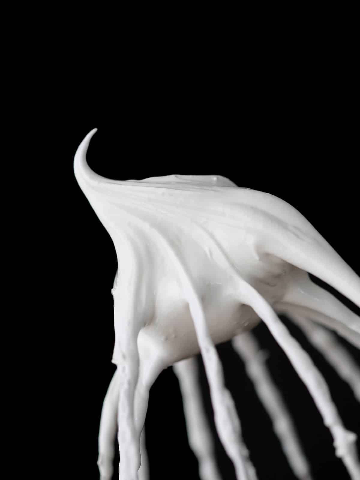 white marshmallow fluff on whisk with black background.
