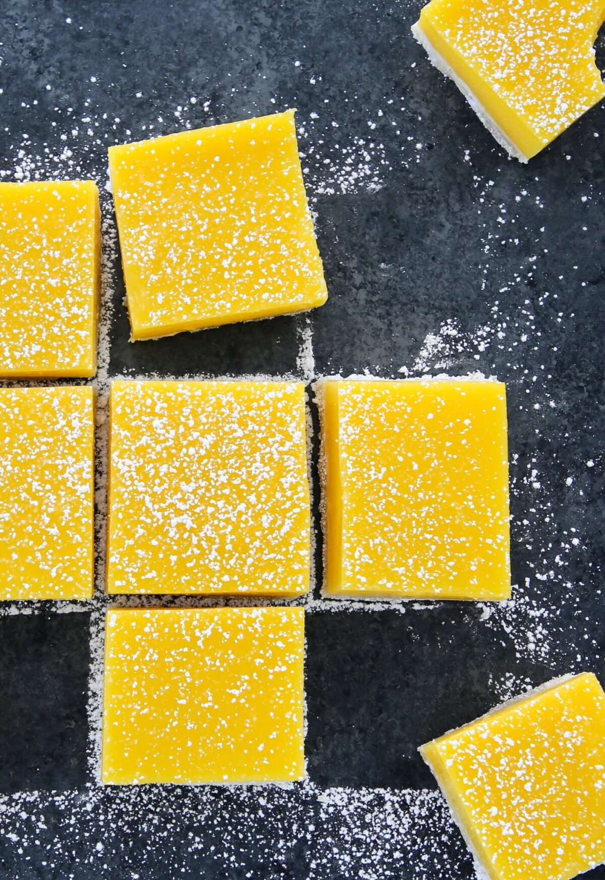 Lemon Bars Confectioners Sugar Scattered on Grey Board.