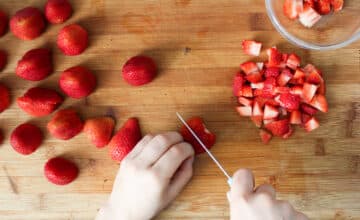 Strawberries being sliced on wooden cutting board