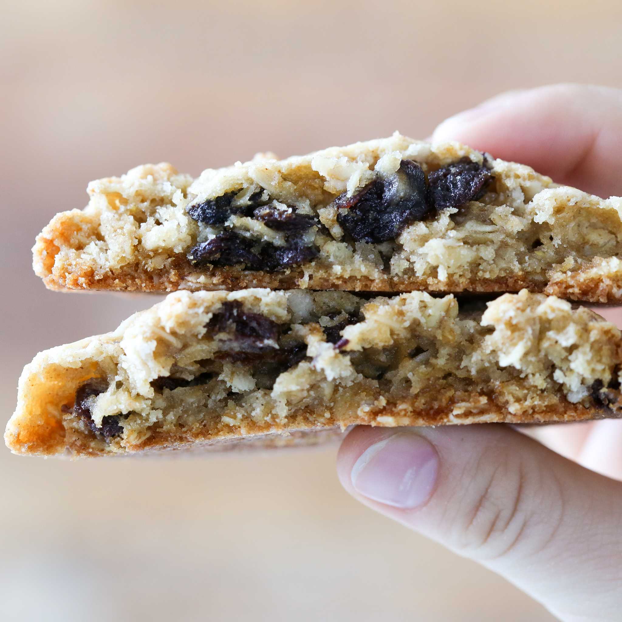 Two oatmeal raisin cookies held in a hand and packed with raisins.
