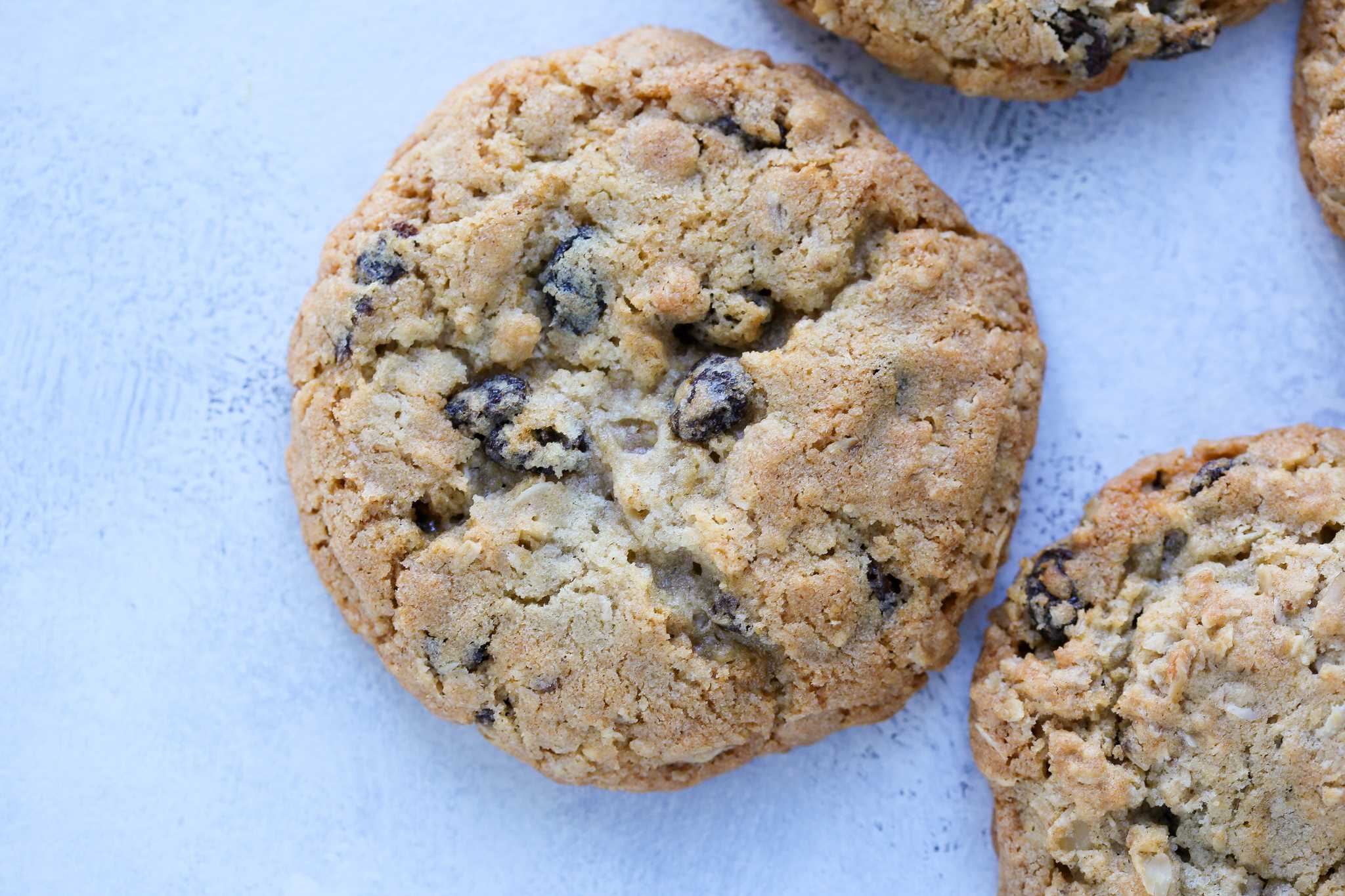 A chewy oatmeal raisin cookie on a light blue background. 