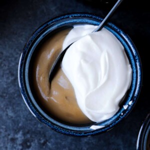 Caramel colored butterscotch pudding in a dark bowl with half of the cover topped with white whipped cream.