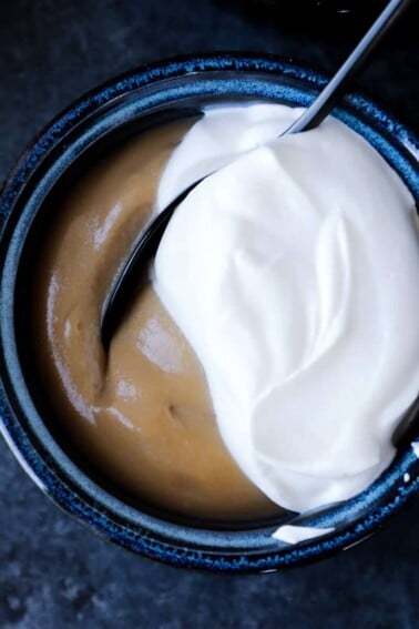 Caramel colored butterscotch pudding in a dark bowl with half of the cover topped with white whipped cream.