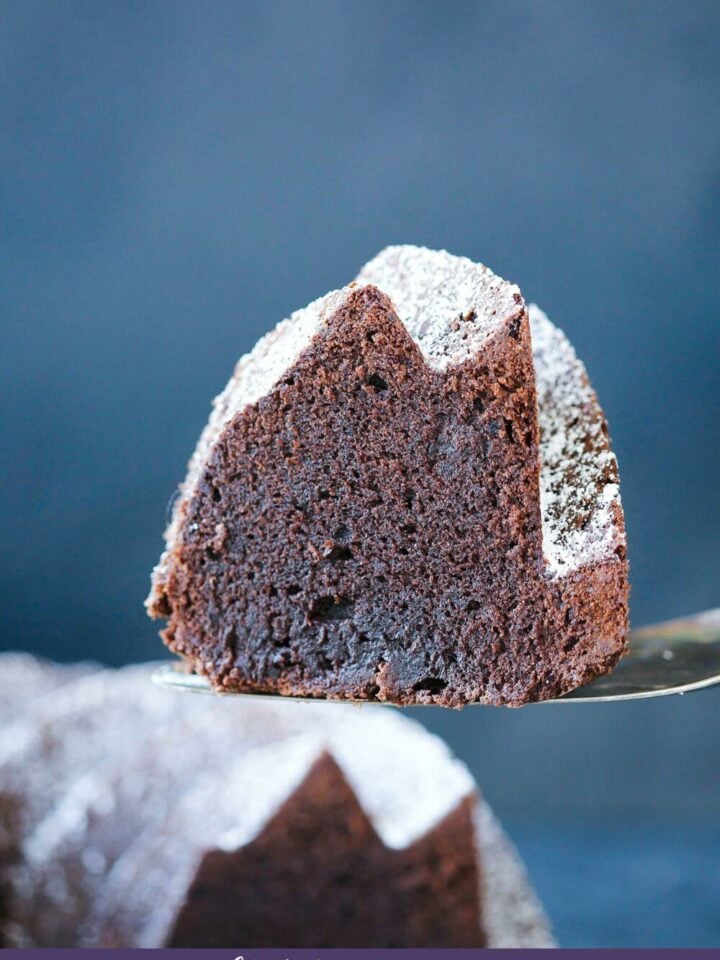 A slice of chocolate pound cake on a server against a blue backdrop.