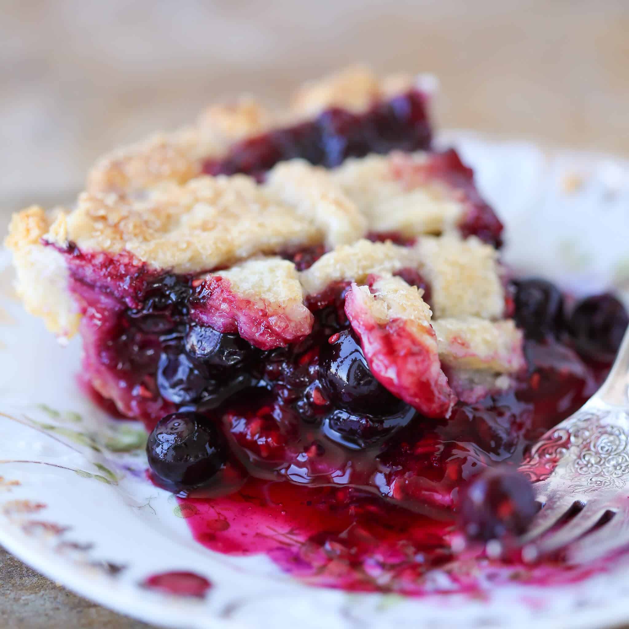 A slice of mixed berry pie on white antique plate.