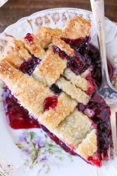 A serving of mixed berry pie with a lattice top and silver fork.